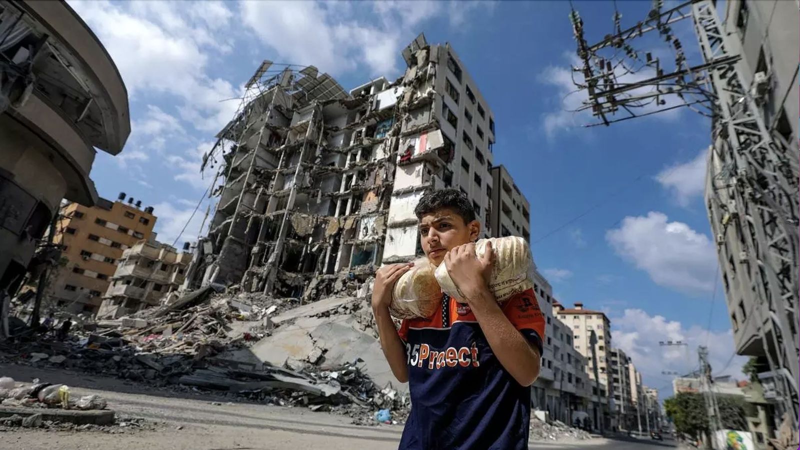 Un joven con dos bolsas de pan camina en una Gaza bombardeada