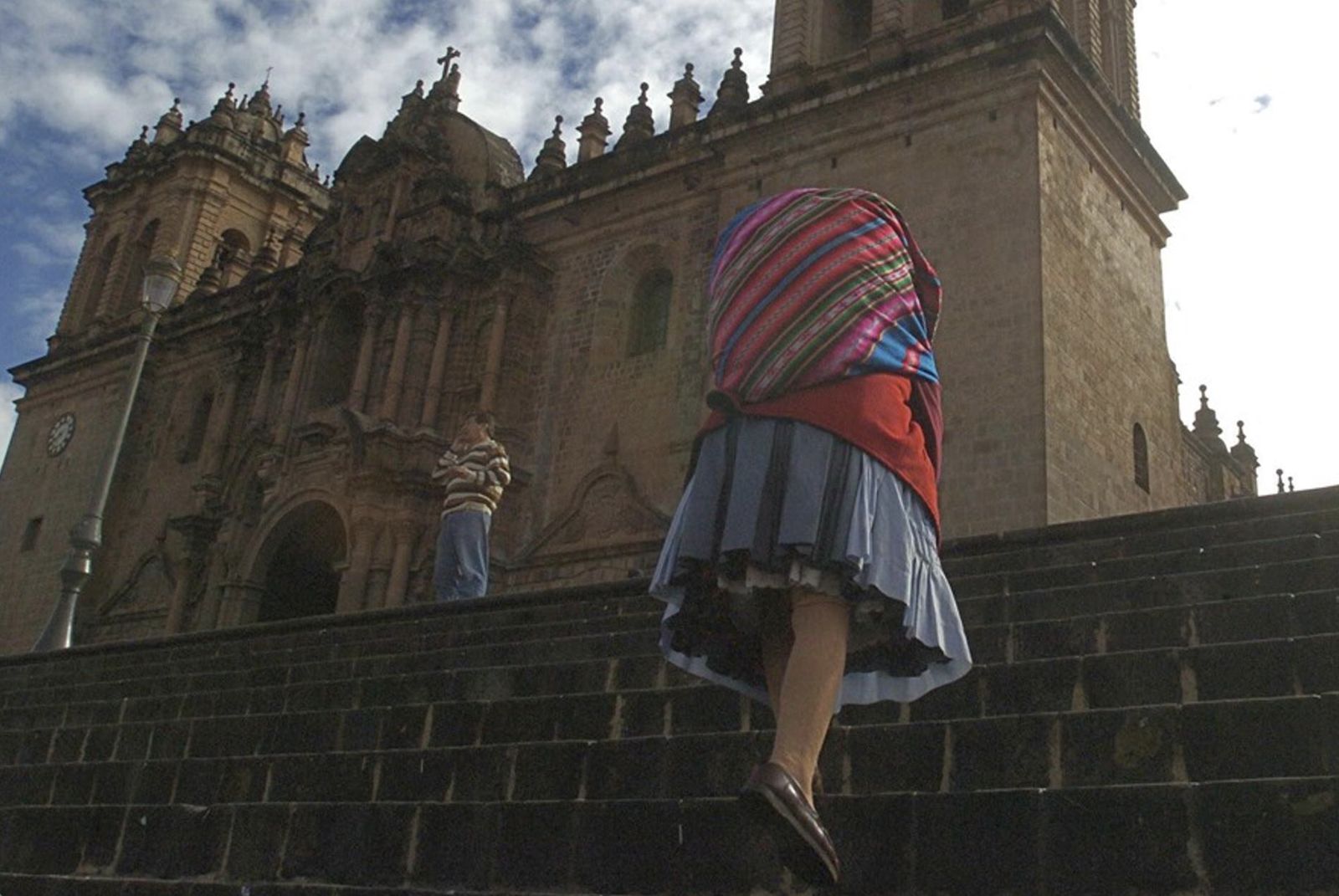Una mujer indígena sube las escaleras ante la catedral de Cuzco