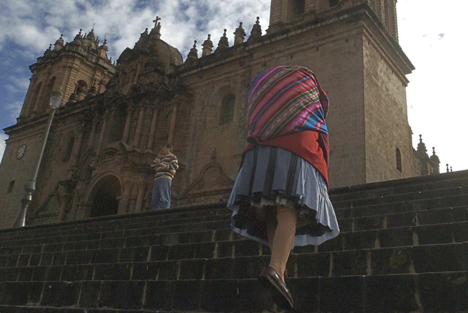 Una mujer indígena sube las escaleras ante la catedral de Cuzco