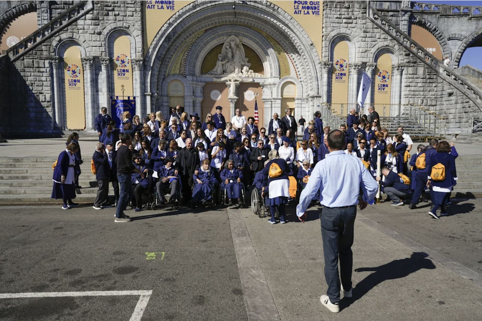 Un grupo de peregrinos ante el santuario de Lourdes con los mosaicos de Rupnik tapados