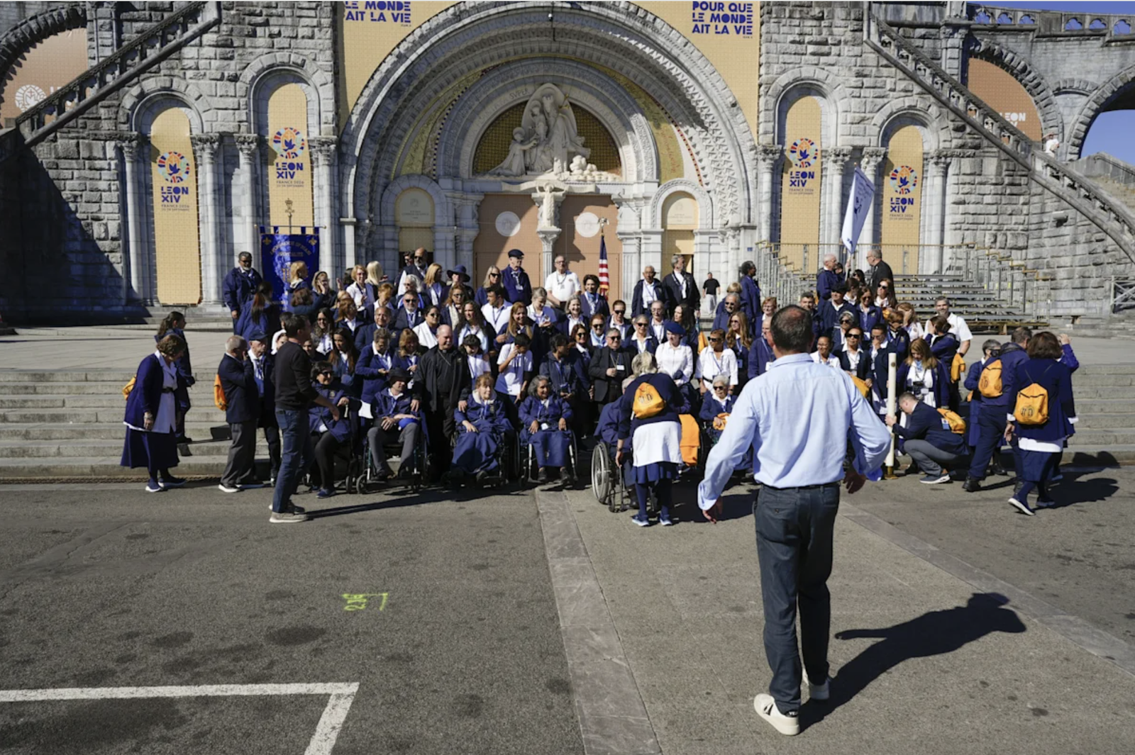 Un grupo de peregrinos ante el santuario de Lourdes con los mosaicos de Rupnik tapados