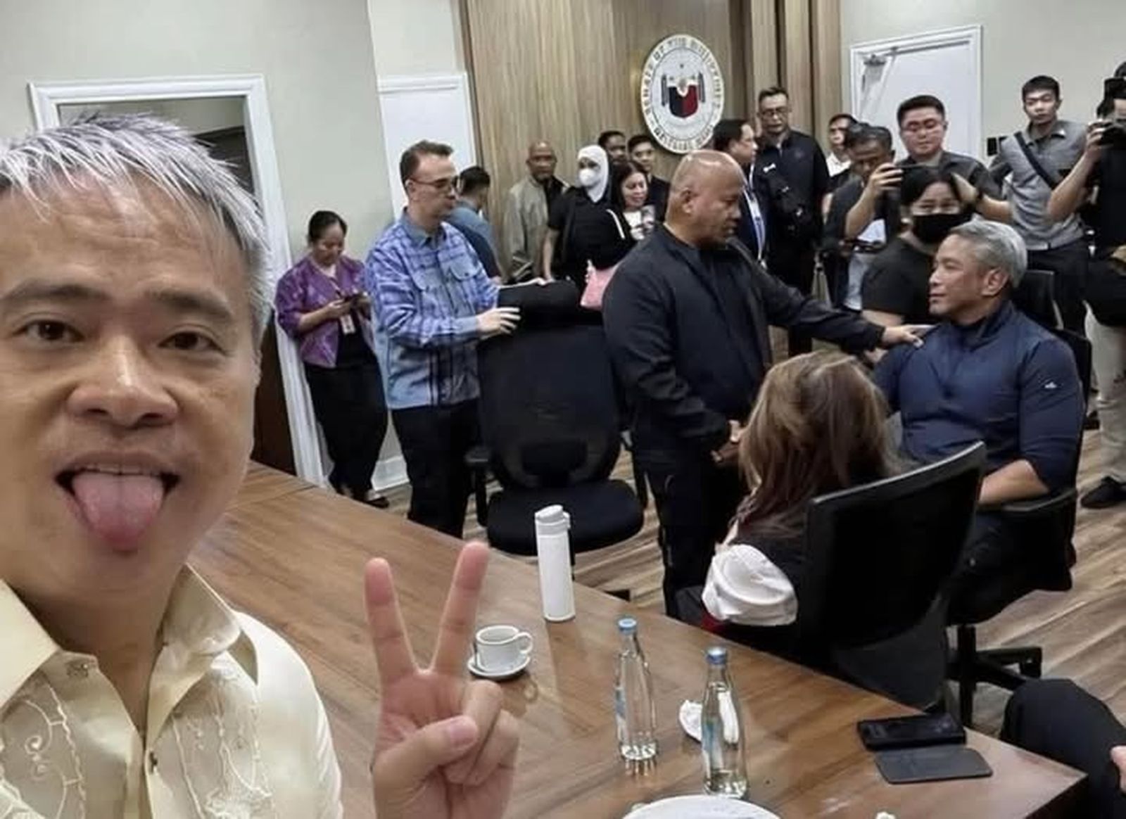 Selfi de un senador que saca la lengua para mofarse del pueblo tras el victorioso montaje en el Senado filipino.  Destaca la calvicie del fugitivo Dela Rosa hablando con un miembro del gabinete del presidente y rodeado de los 13 Judas