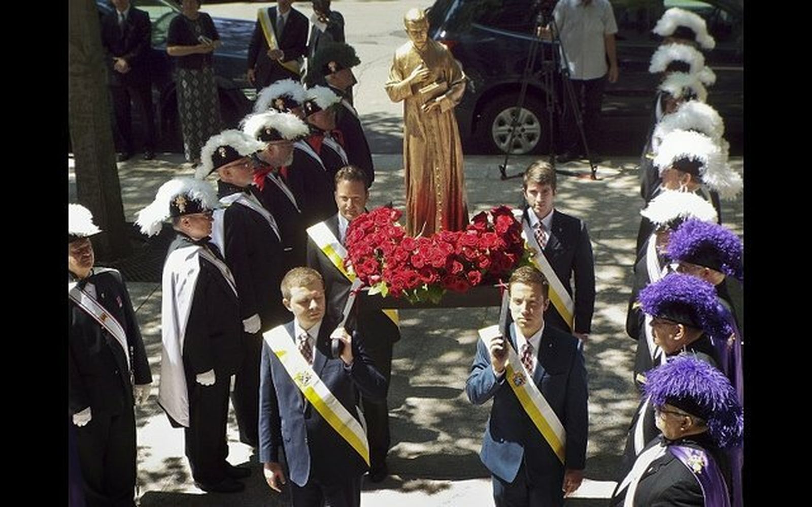 Cuatro hombres llevan una estatua de Padre Michael McGivney pasando una guardia de honor