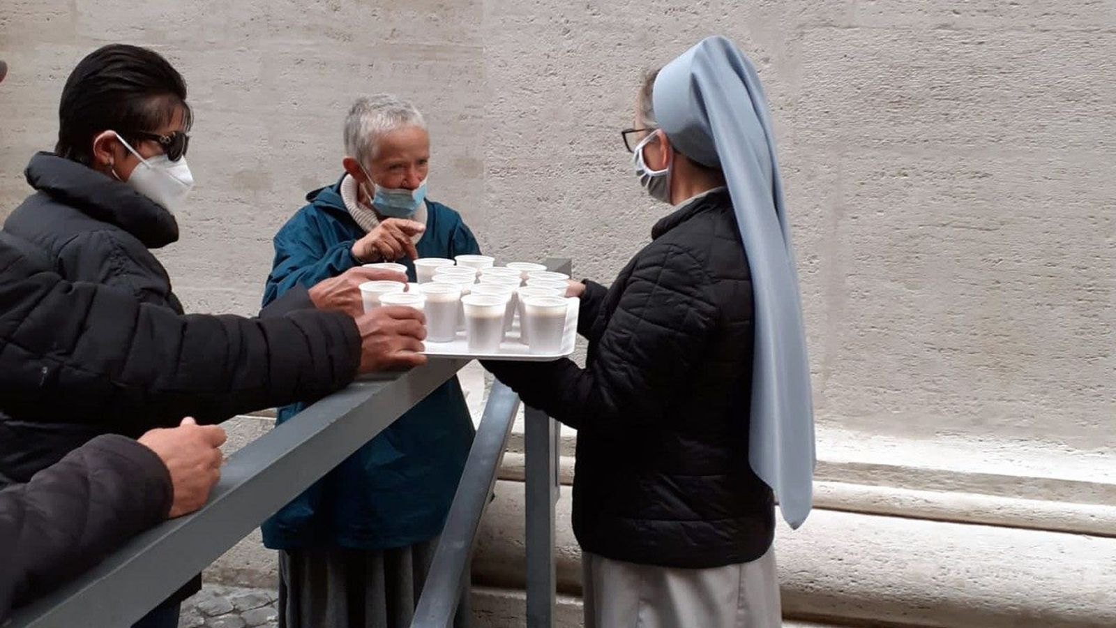 Distribución de bebidas a las personas necesitadas en espera de ducharse bajo el columnado de San Pedro
