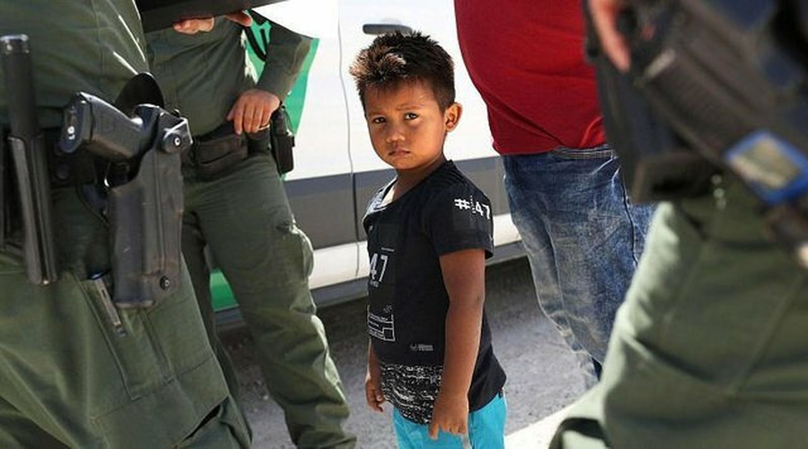 Un niño migrante rodeado de agentes fronterizos