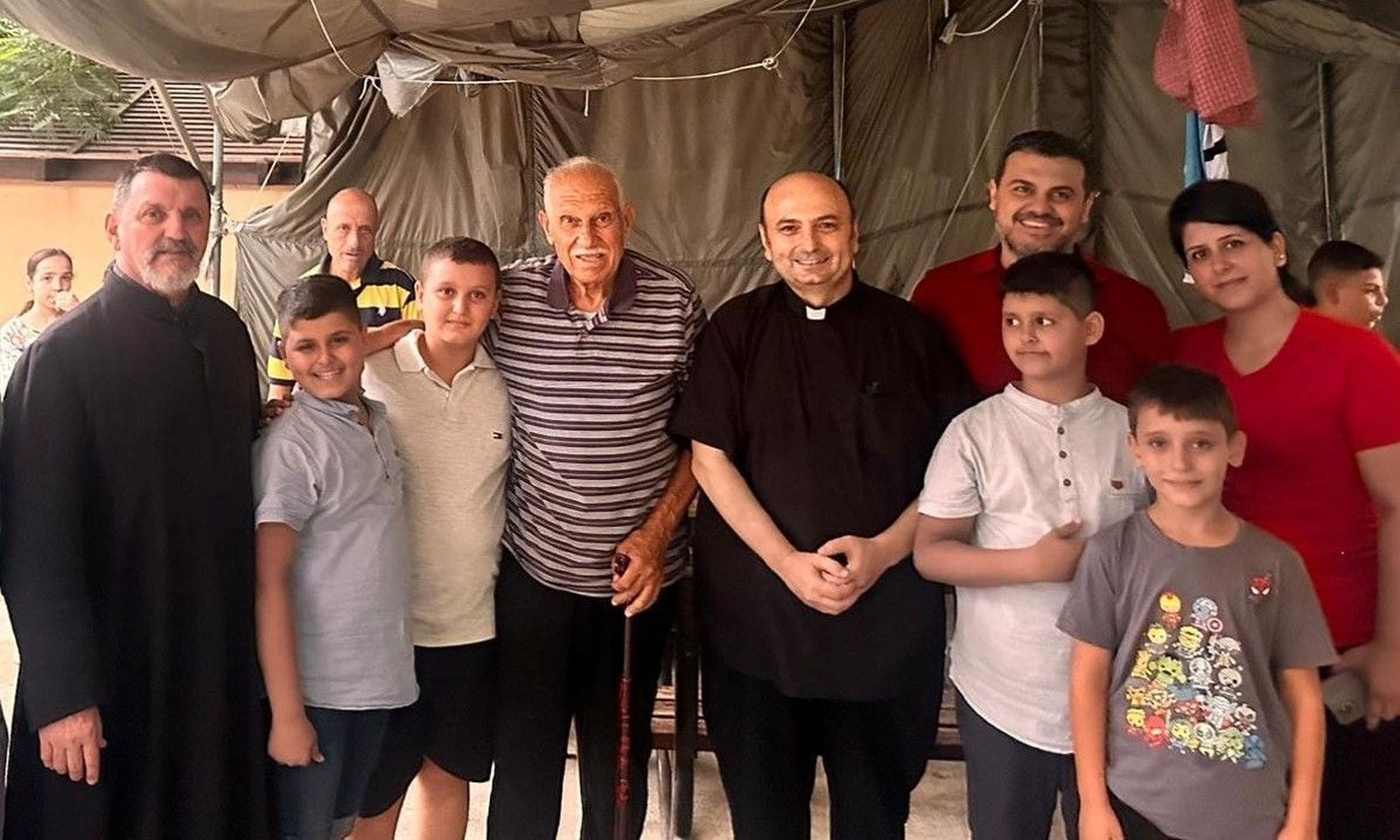 El párroco posa junto a algunos refugiados en el exterior de la iglesia de la Sagrada Familia en Gaza