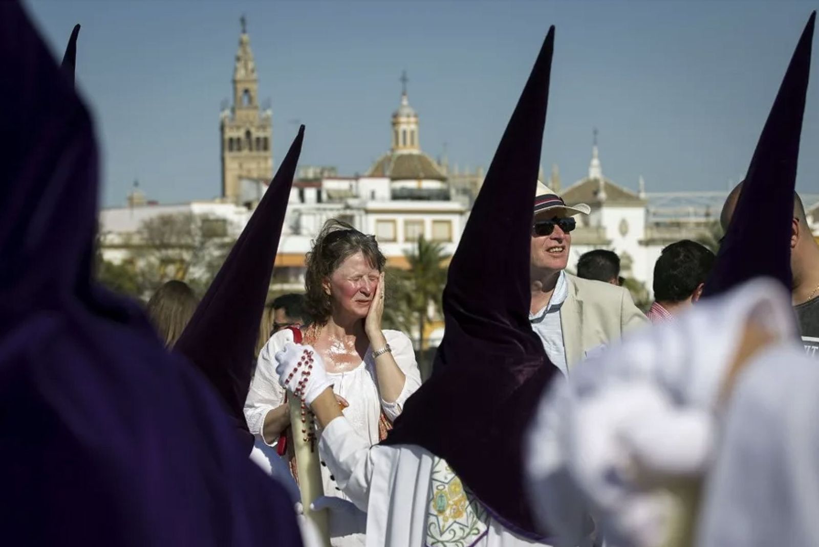 Unos turistas contemplan el paso de los nazarenos en Sevilla