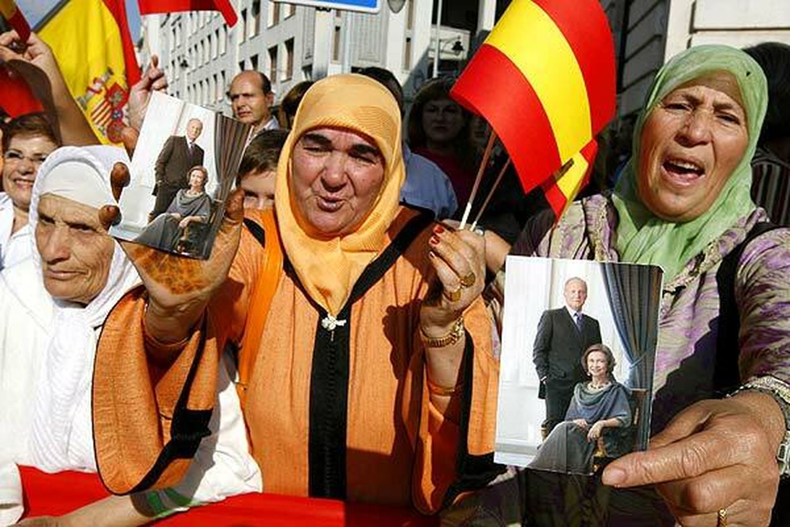 Musulmanas españolas sosteniendo banderas y fotos de la Familia Real